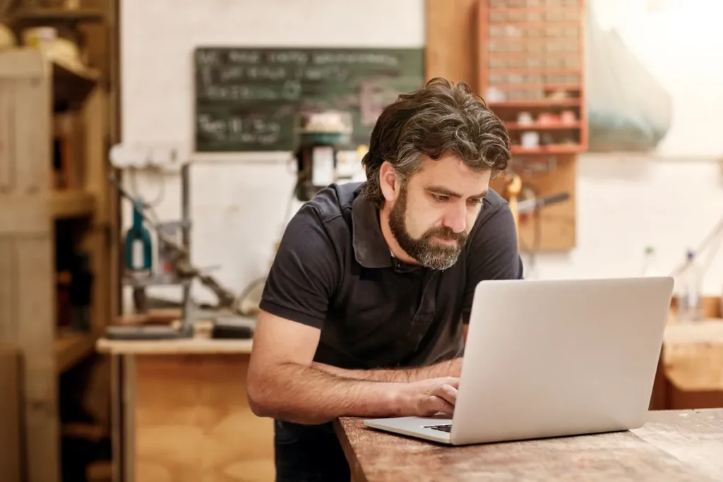 Self-employed business owner reviewing his finances on a laptop in his workshop